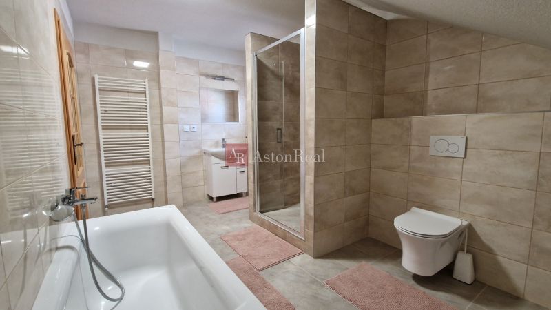 A bathroom in a family house with a bathtub, a shower corner, and beige tiles.