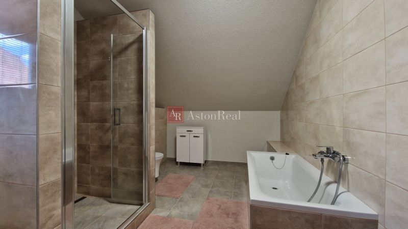A bathroom in a family house with a bathtub, a shower corner, and light tiles.