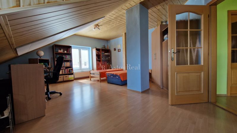 Attic room of a family house with a desk, sofa, and wooden decor flooring.