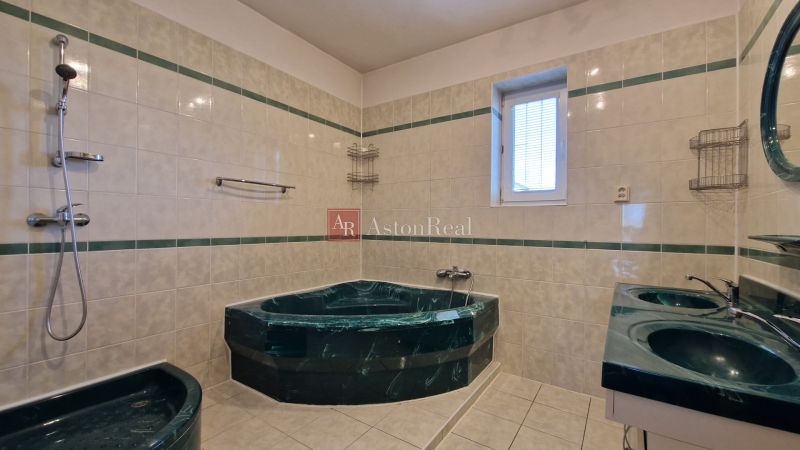 A bathroom with a corner bathtub and double sink in a family house, tiled.
