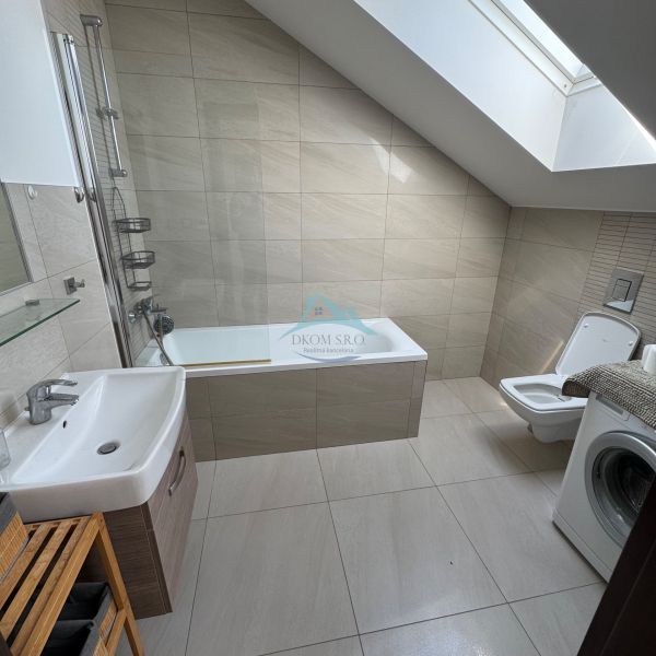 A bathroom in a family house with a bathtub, sink, toilet, and washing machine under a skylight.