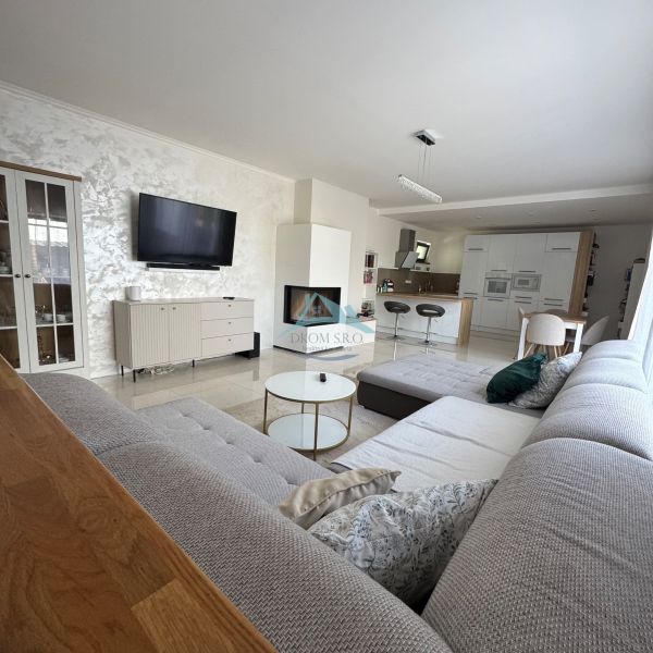 A spacious living room in a family house with a corner sofa and a kitchen counter.