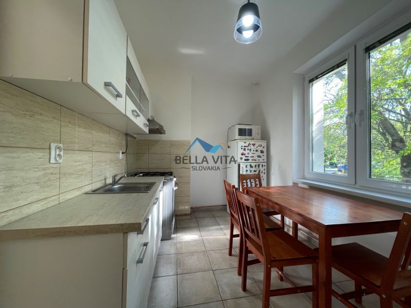A kitchen in a 2-room apartment with a dining table, white cabinets, and tiles.