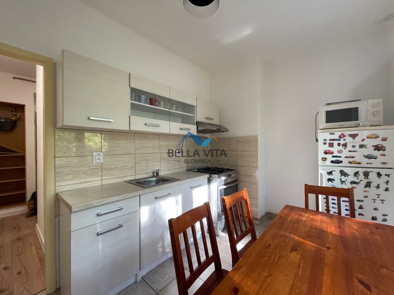 A kitchen in a 2-room apartment with a white kitchen unit and a wooden table.