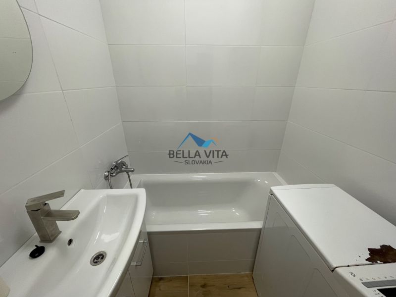 Bathroom in a 2-room apartment with a bathtub, sink, and washing machine, tiles on the walls.