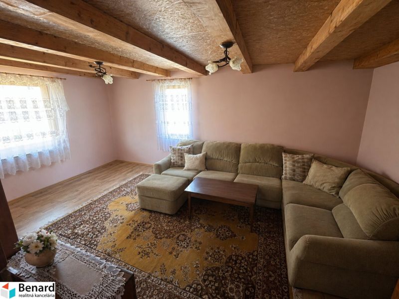 Living room in a family house with a sofa, wooden-patterned floor, and a floral carpet.