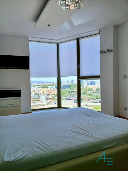 A bright bedroom in a 2-room apartment with a view of the city from large windows.