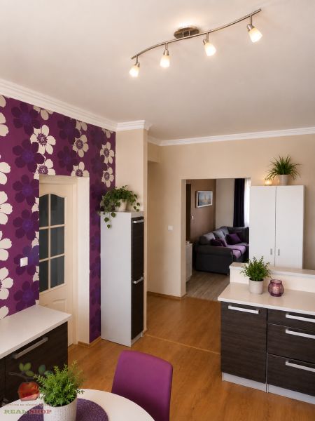A kitchen in a 3-room apartment with a wooden decor floor and floral wallpaper.