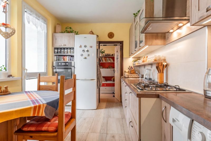 A kitchen in light shades with built-in appliances, a dining table, and a decorated wall.
