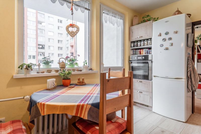 A kitchen in a 3-room apartment with a corner window, a dining table, and a white refrigerator.
