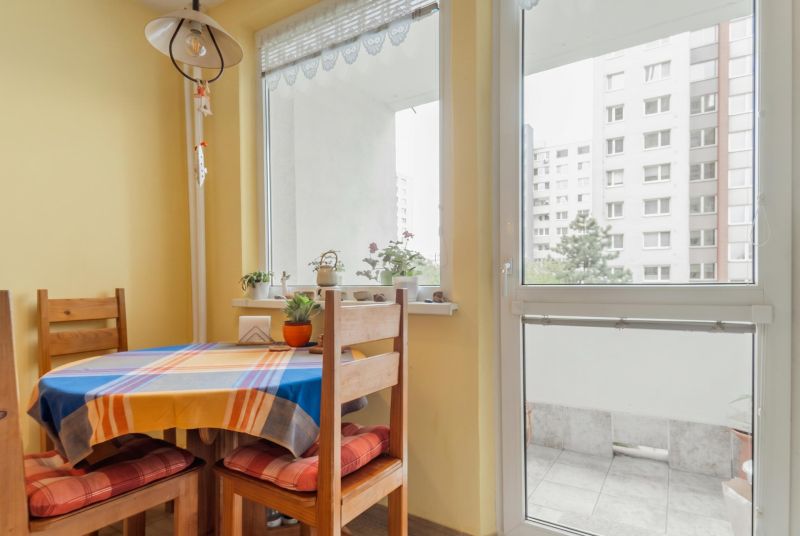 Dining area with a wooden table and chairs near the balcony in a 3-room apartment.