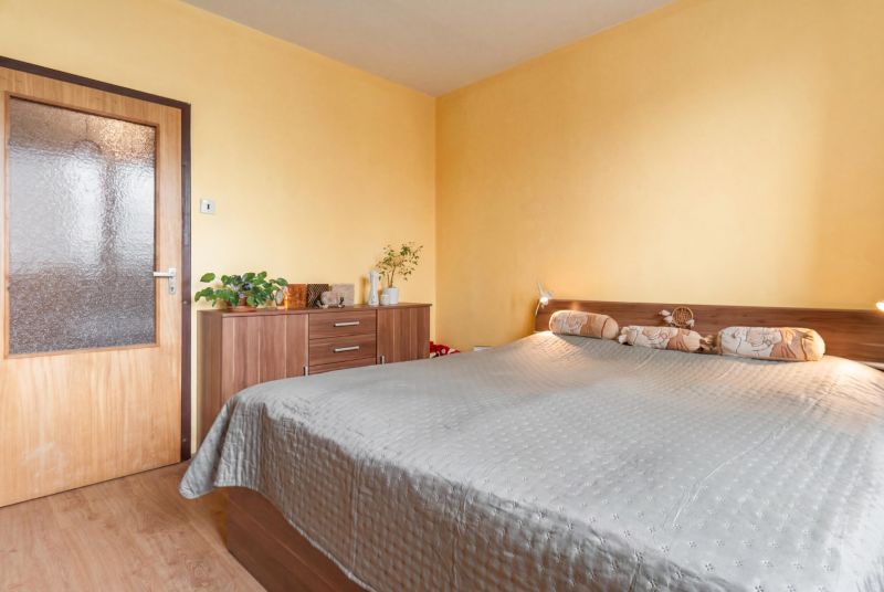 A bright bedroom with a bed, shelf, and wood-decor flooring in a 3-room apartment.