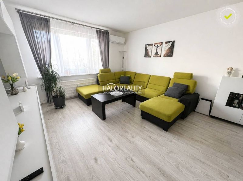 Living room of a 3-room apartment with a sofa, large window, and wood-patterned flooring.