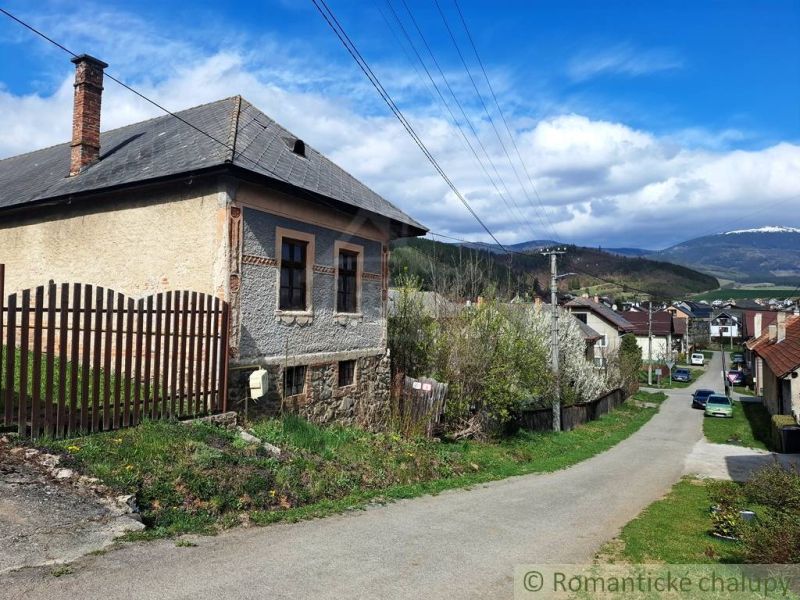 Unusual properties in Heľpa, an older house by a country road, hills in the background.