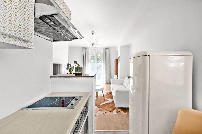 A kitchen with a white fridge, a stove, and a view of the living room in a two-room apartment.