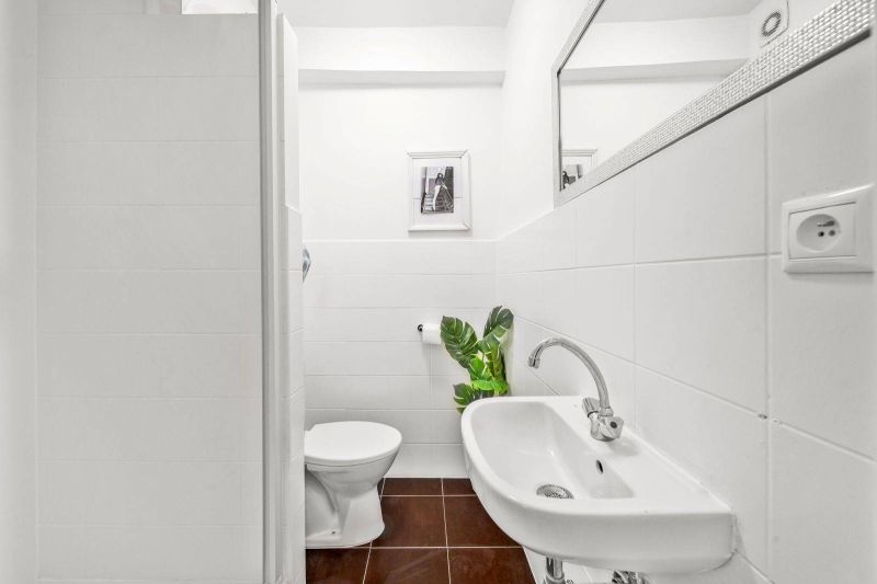 Bathroom of a 2-room apartment with a sink, toilet, and brown tiles.