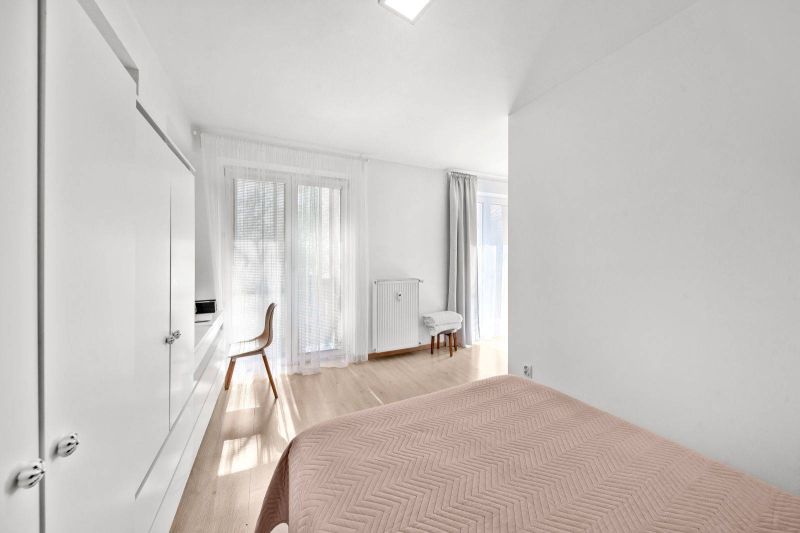 A bright bedroom with wood-patterned flooring and simple furniture in a 2-room apartment.