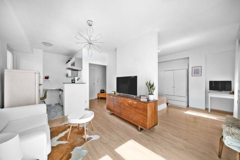 Living room in a 2-room apartment with a TV, the space is bright, flooring with wooden decor.