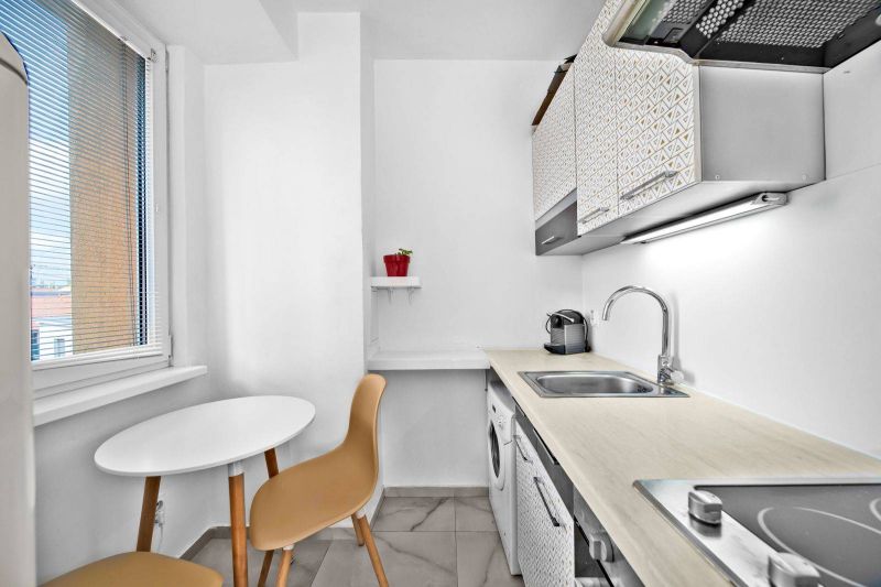A kitchen of a 2-room apartment with a window, white furniture, and a table with chairs.