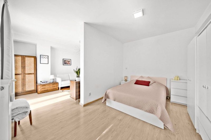 Bright bedroom in a two-room apartment with wood-patterned flooring and cozy furniture.