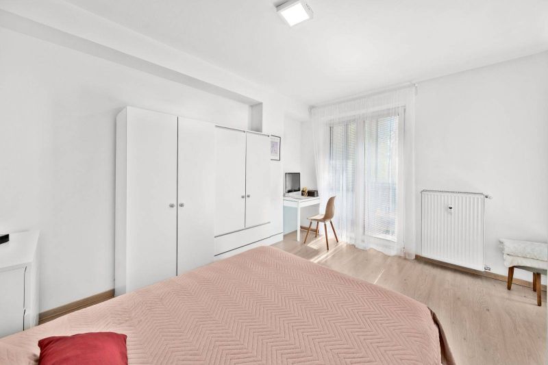 Bedroom in a two-room apartment with white furniture and a wood-patterned floor.