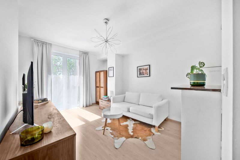A bright living room in a two-room apartment with wood-patterned flooring and a white sofa.