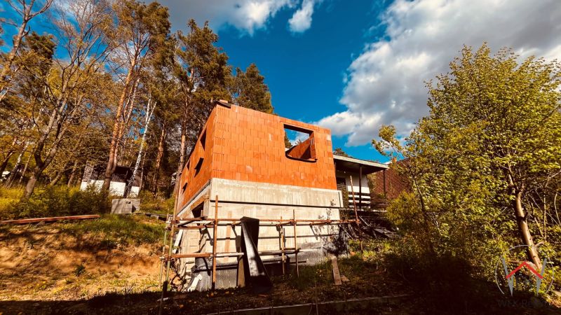 A cottage construction in the recreational area of Nová Kelča surrounded by trees and a blue sky.