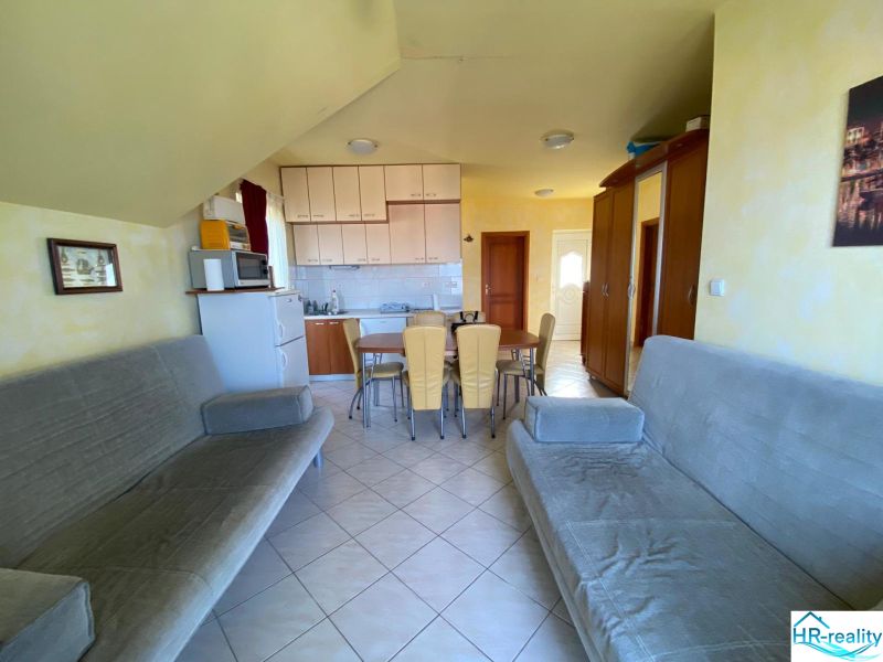 Living area with sofas, kitchen, dining table, and ceramic tiles in a holiday apartment.