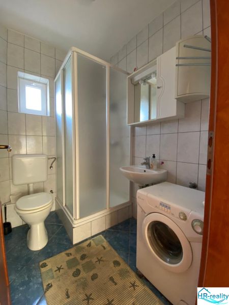 Bathroom in a holiday apartment with a washing machine, shower, and toilet.