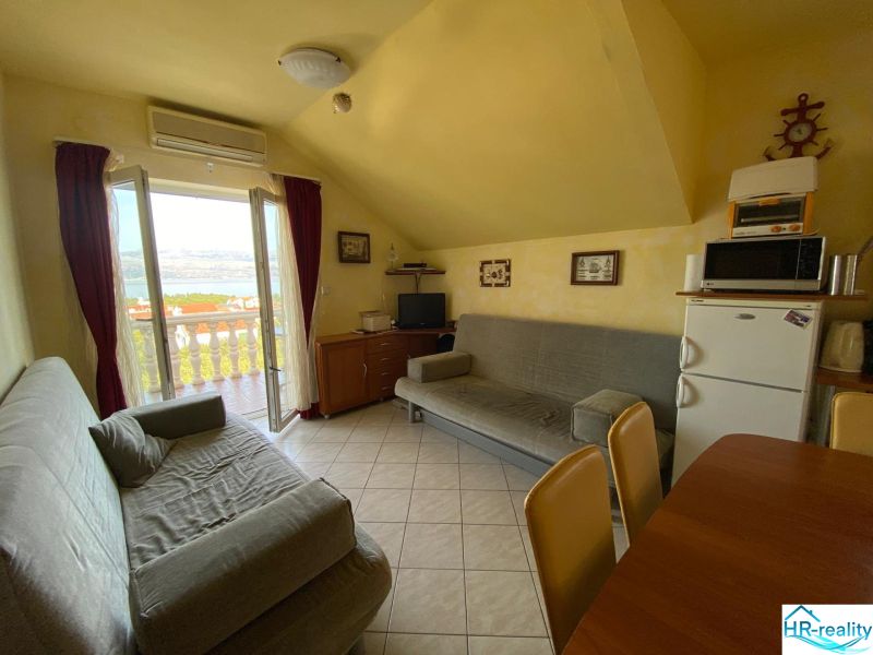 Living area of the Holiday Apartment with sofas, refrigerator, and balcony view of the sea.