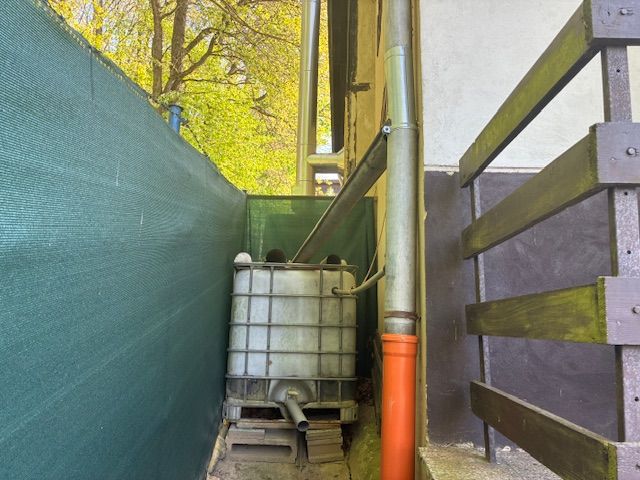 Under the cottage in Ilava, there is a plastic water tank with drainage and green fencing.