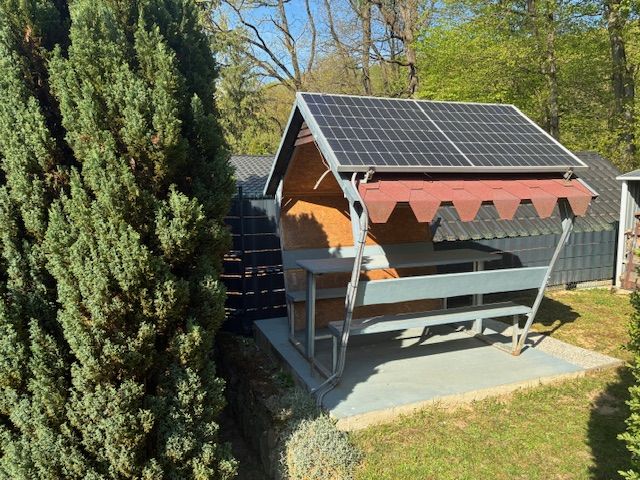 A cottage in Ilava with a gazebo and a solar panel in a garden surrounded by trees.