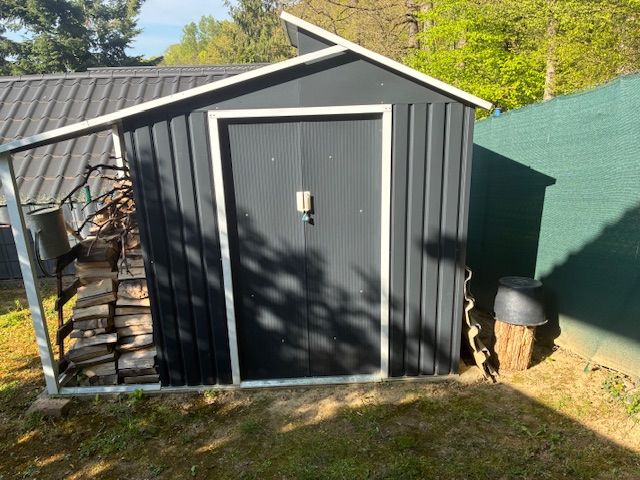 A garden with a tin shed in Ilava, next to which firewood is stored.
