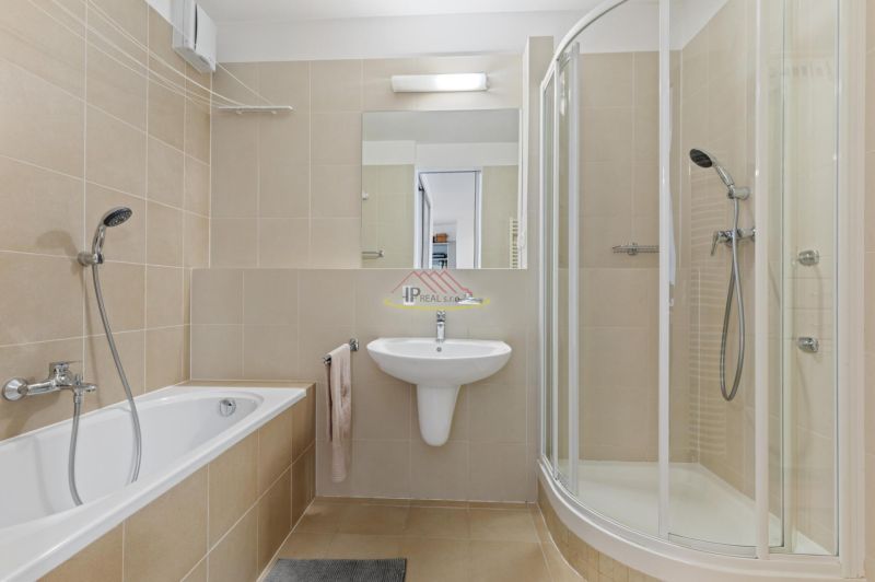 Bathroom with a bathtub, shower, sink, and mirror in a 2-room apartment.