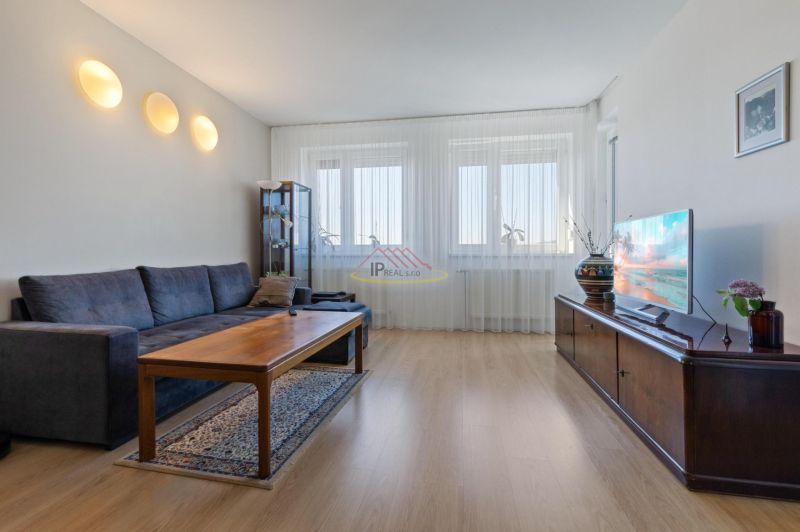 Living room in a two-room apartment with a sofa, table, and wooden decor flooring.