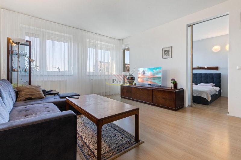 Living room of a two-room apartment with a sofa, table, and television on wooden furniture.