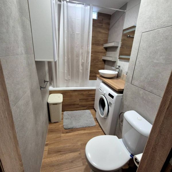 Bathroom in a 3-room apartment with a bathtub, washing machine, and floor with wooden decor.