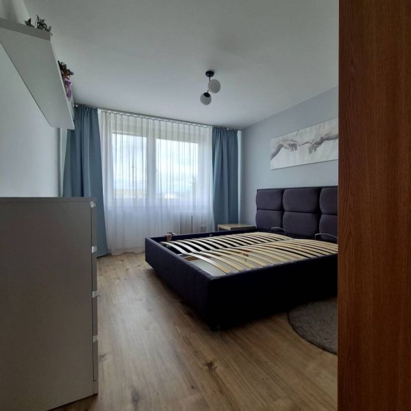 A bedroom with a gray bed, curtains, and a wooden decor floor in a 3-room apartment.