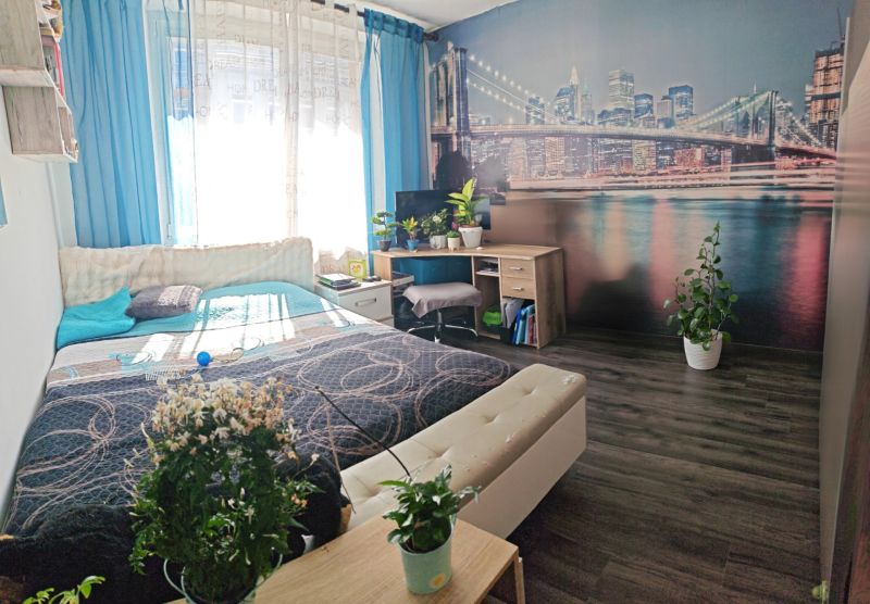 A bedroom in a 3-room apartment with a wooden decor floor and a city photo wallpaper.