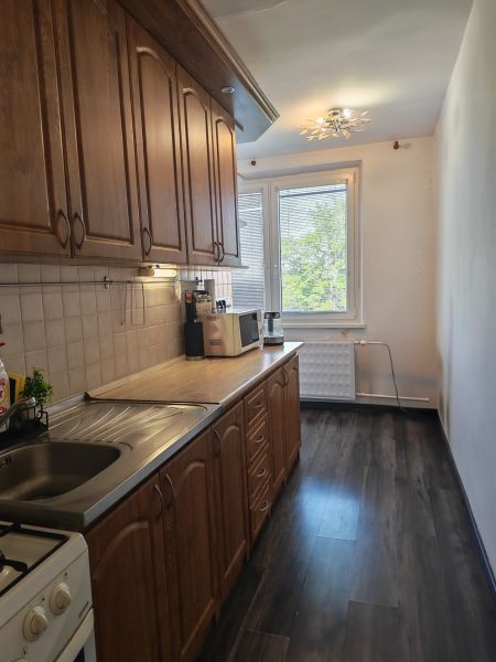 A kitchen in a 3-room apartment with a wooden decor floor and a wooden kitchen unit.