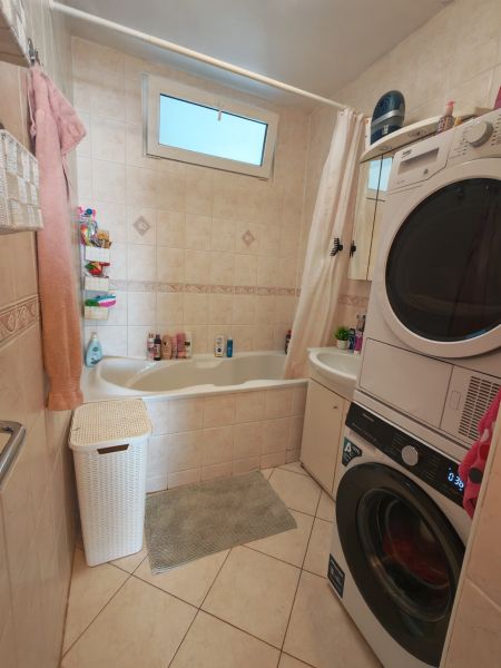 Bathroom with a washing machine in a 3-room apartment, with a bathtub and a window, tiled floor.