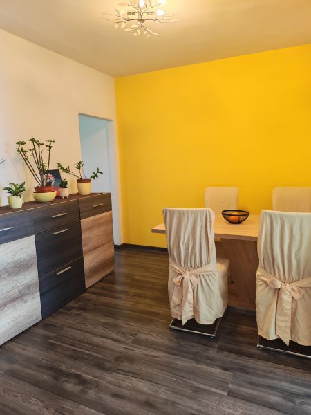 A dining room with a wood-patterned floor and a yellow wall in a three-room apartment.