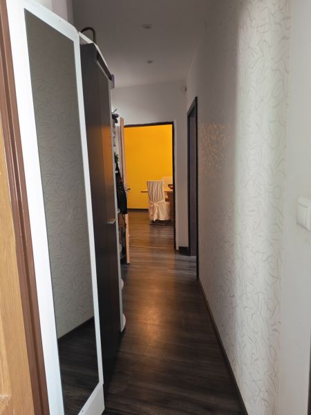 A hallway in a 3-room apartment with a wooden decor floor and a mirror on the wall.