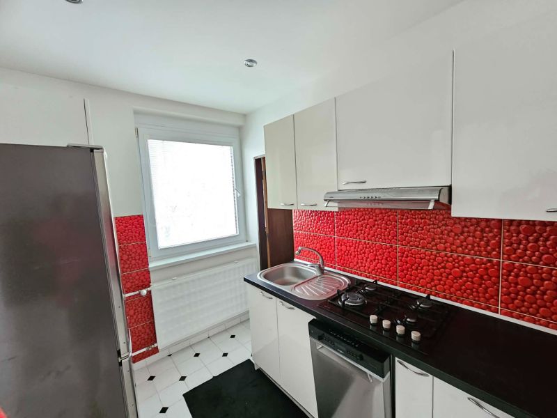 A kitchen with white cabinets and red tiles in a 3-room apartment.