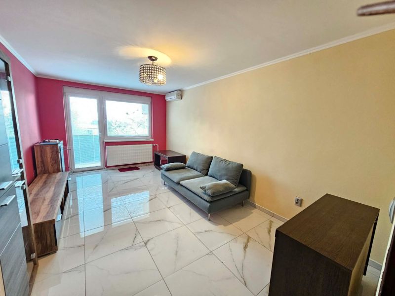 Living room of a three-room apartment with glossy tiles, a sofa, and a red wall.