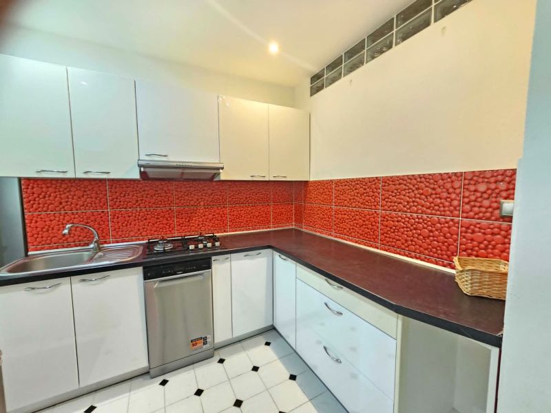 A kitchen with white cabinets, red tiles, and stainless steel appliances in a three-room apartment.