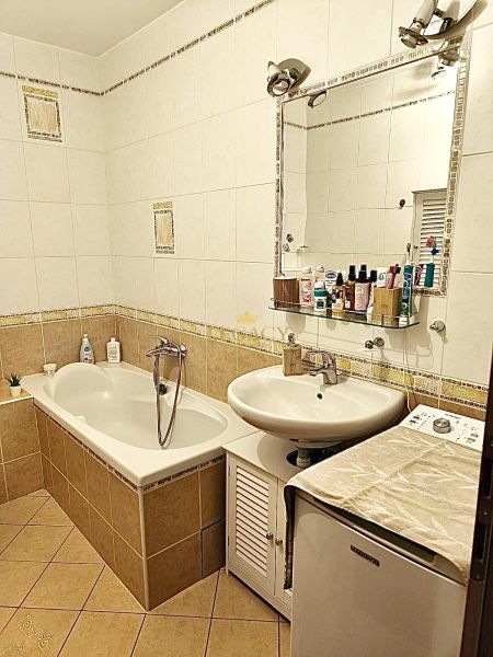 A bathroom in a 3-room apartment with a bathtub, a sink, and a mirror full of cosmetics.