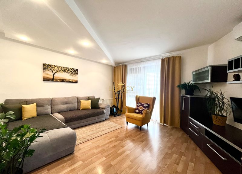 Living room in a three-room apartment with a corner sofa, wooden decor flooring, and a yellow armchair.