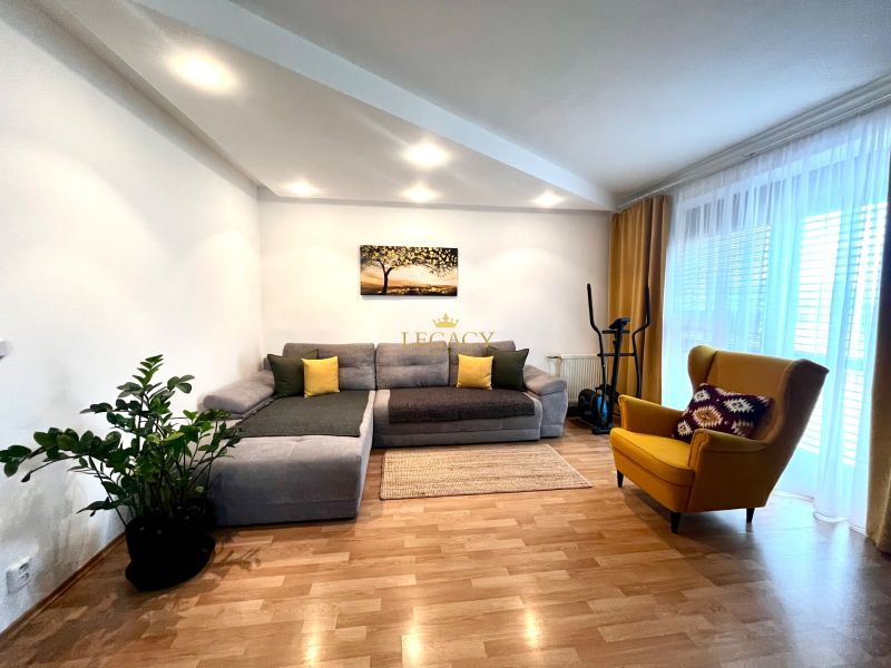 Living room of a three-room apartment with a wooden decor floor, gray sofa, and yellow armchair.