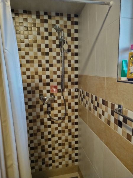A shower enclosure in a family house with a tiled pattern and a shelf for cosmetics.